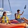 Three people kayaking near a sailboat