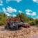 3 people in an open air 4 by 4 vehicle driving through mud