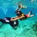 Three people snorkeling underwater behind power sea scooters