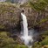 A large waterfall pouring through a rock face onto a valley below
