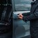 A man in professional driver attire gesturing with his hand toward the open door of a van