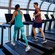 A woman and man chatting while walking on treadmills inside a fitness center