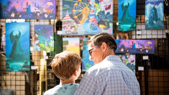 An adult and child gazing at artwork on display featuring various Disney characters