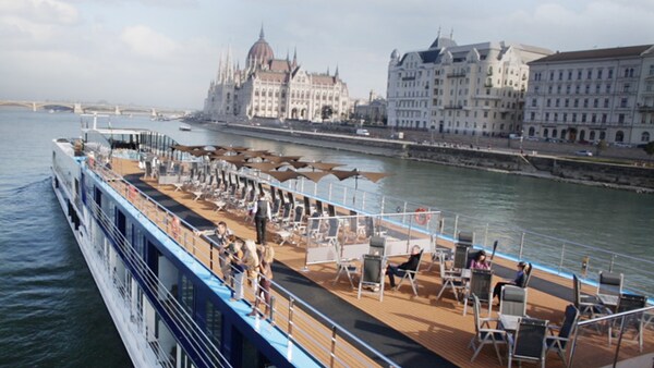 On a European adventure, Guests on the deck of a vessel look at the scenery as they cruise along