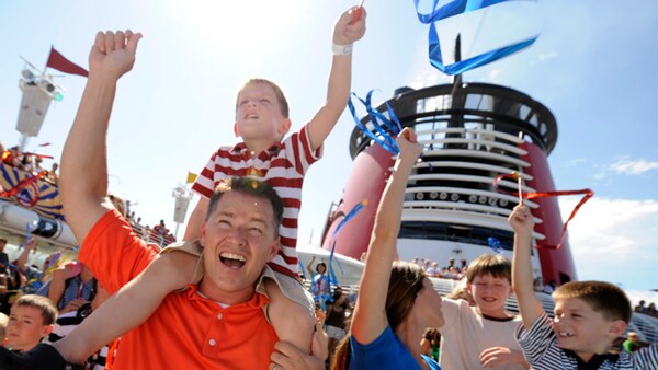 Smiling Disney Cruise Line Guests wave happily from the deck of the ship before setting sail