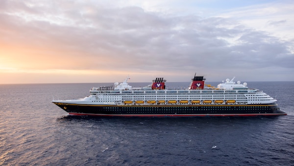 A Disney Cruise Line ship sails smoothly through calm waters, at sunset