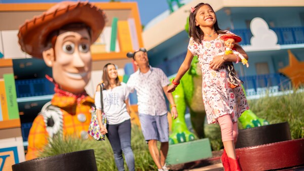 A couple and their child in front of a large figure of Woody from the film, Toy Story, at Disney’s All Star Movies Resort