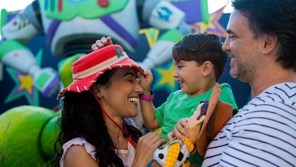 A smiling couple holds their young child between them at the Toy Story play area at Disney’s All Star Movies Resort
