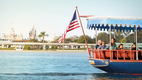 Guests on a boat in the water at Walt Disney World Resort, with the monorail and Cinderella Castle in the distance