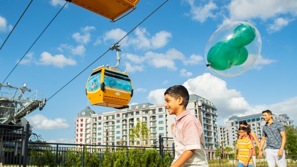 A family of 4 walking below a Disney Skyliner aerial gondola near Disney’s Riviera Resort