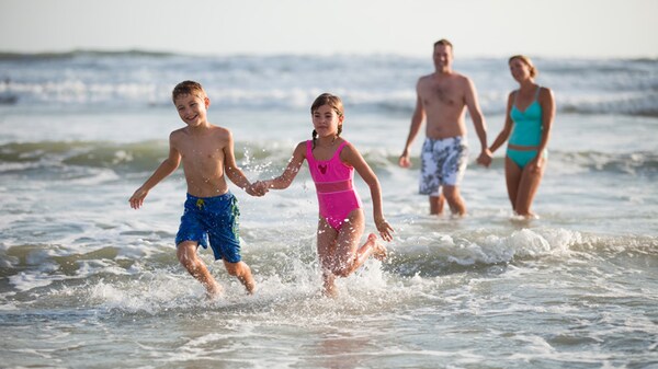 A little boy and girl hold hands and splash through the small waves as their parents look on