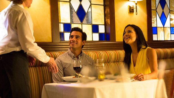 A couple sitting at a dinner table, speaking to a server