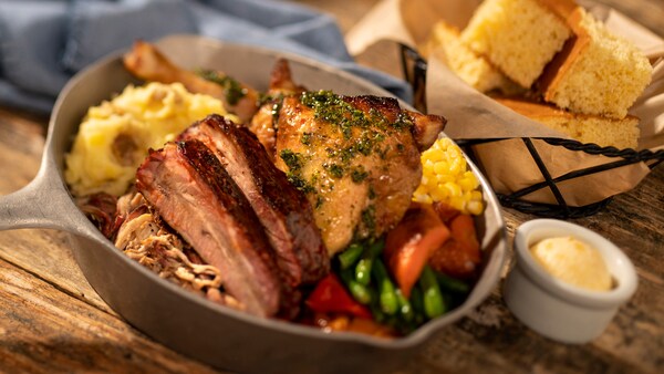 A basket of cornbread and a skillet with brisket, chicken, mashed potatoes, green beans and corn