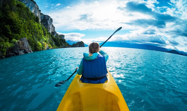 A kayaker dips a paddle in the water, near a scenic, rocky coastline 