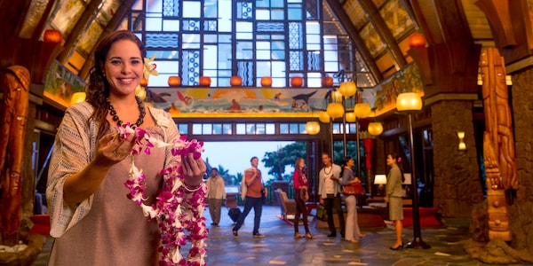 A female Cast Member standing in the Aulani Resort lobby, welcoming new Guests with lei necklaces