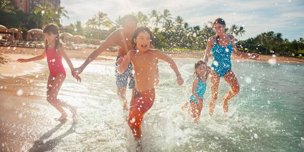 A couple and their 3 children run playfully along the beach where it meets the water
