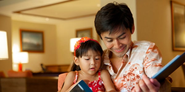 A man in a Hawaiian shirt reads a book to his young daughter