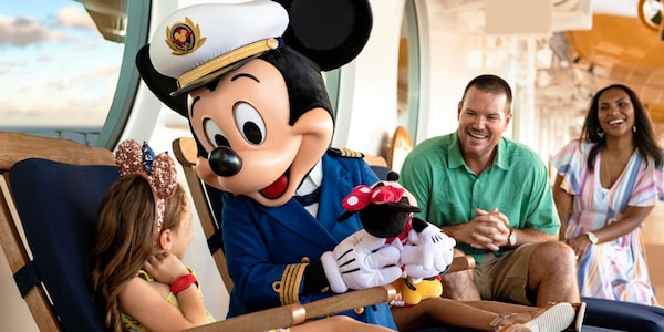 Aboard a Disney Cruise Line ship, Mickey Mouse interacts with a delighted young Guest as her parents look on