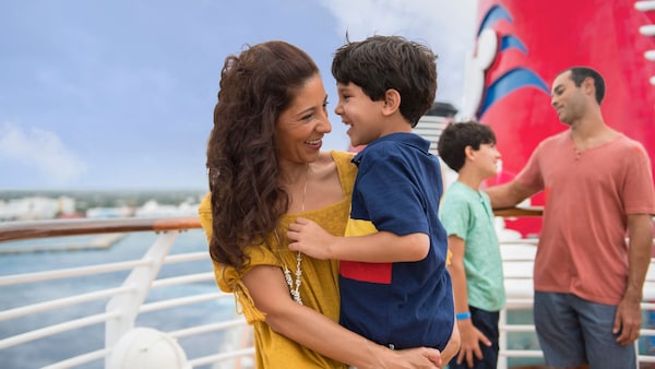 On the deck of a Disney Cruise Line ship, a mother holds her smiling young son, as the father engages with his older son