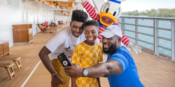 On the deck of a ship, a father and his 2 sons take a selfie with Donald Duck 