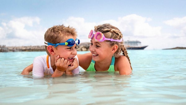 Two young children wearing goggles exchange smiles as they play in shallow water