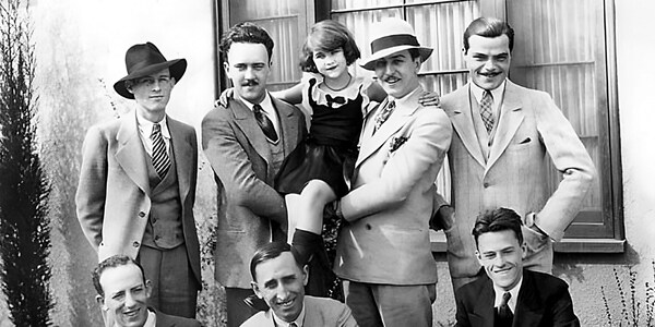 A photograph from the 1940s with 7 men wearing suits, including Walt Disney and his brother Roy, and 1 girl
