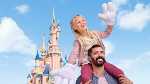 A young girl wearing Mickey Mouse gloves sitting on her father’s shoulders near Cinderella Castle at Walt Disney World Resort