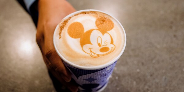 A Cast Member holding a cup of coffee with Mickey Mouse drawn on the foam