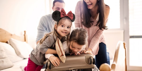 A family of 4 on a hotel bed attempting to close a packed suitcase