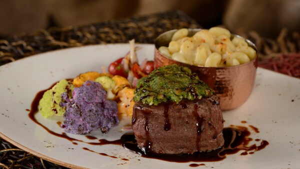 A serving of filet mignon served on a plate with macaroni and vegetables