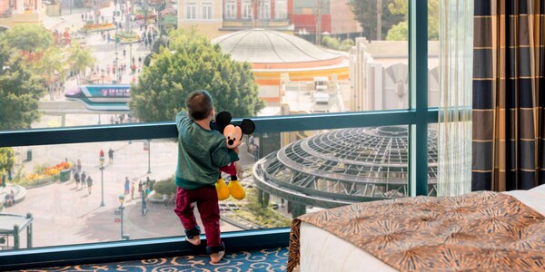 A rendering of a young boy holding a Mickey Mouse plush looking out the window at the Disneyland Hotel 