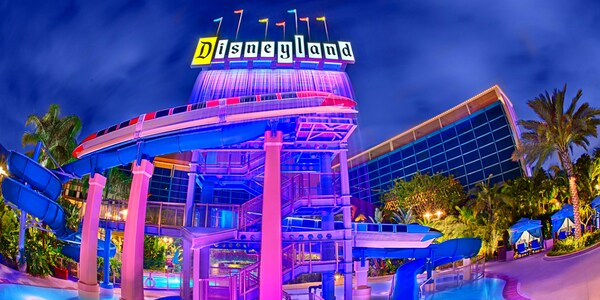 The Monorail waterslide and waterfall glow at night over the pool  area surrounded by hotel towers