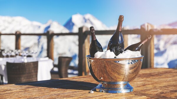 Bottles of champagne cool in a bowl of ice at an outdoor restaurant, with scenic mountains in the background