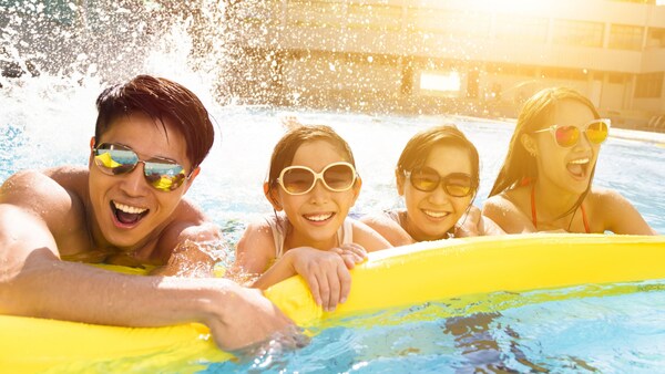 A smiling family holds onto a pool raft as they enjoy the water