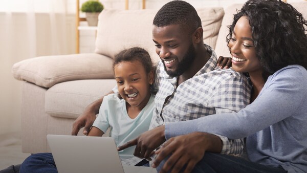 Two parents and their child sit on the floor looking at a laptop