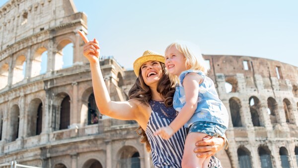 A mother holds her young daughter as they stand before the iconic Colosseum in Rome, Italy