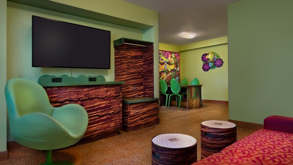Interior de um quarto com piso laminado, 4 cadeiras, uma cadeira estofada, 2 bancos, uma mesa, uma cama embutida, um sofá, uma TV de tela plana com suporte de parede, uma cômoda e um guarda-roupa