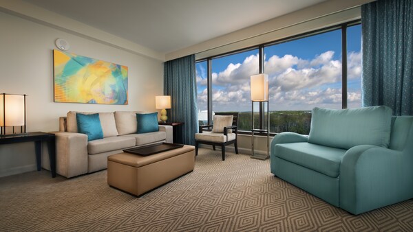 Un área de estar con un sofá, una otomana, una silla, un cuadro, un sofá de dos cuerpos y una ventana con vista al lago