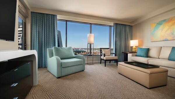 Una habitación con un sofá de dos cuerpos, un sofá, una otomana, un TV, cajones, un cuadro, una silla, 2&nbsp;lámparas y una ventana