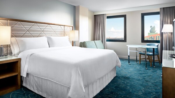 Quarto com cama, travesseiros, sofá de dois lugares, mesa, cadeira, cortina e vista para o Walt Disney World Swan Hotel