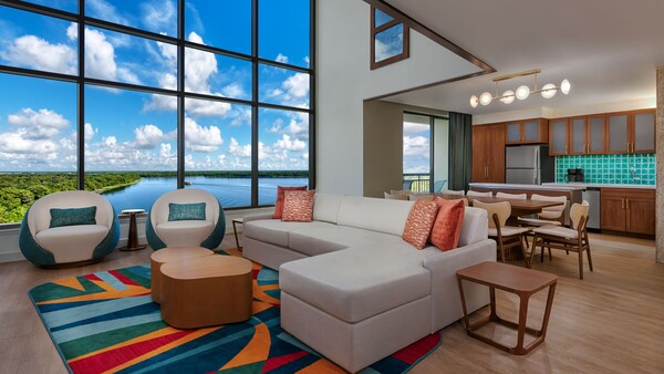 Una sala de estar de una villa grande de lujo de 3 dormitorios con un estudio y vista preferencial en Bay Lake Tower at Disney's Contemporary Resort, con un sofá, 2 sillas, una mesa de restaurante, una cocina y una ventana con vistas a Bay Lake