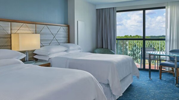 Um quarto de hotel com 2 camas de casal, uma mesa com cadeira e uma varanda no Walt Disney World Dolphin Resort