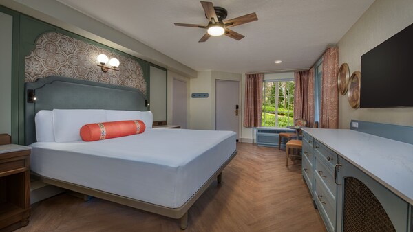 Una habitación de hotel de Disney's Port Orleans Resort con una cómoda, TV, ventilador de techo, cama, dos mesas de noche, dos sillas y una mesa