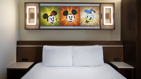 Choosing the perfect resort room category walt disney world all star Preferred Room with lit up artwork of animated Disney Characters, above a bed