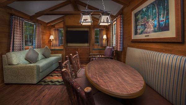 A rustic dining table in front of a lodge chair, a sofa with throw pillows and a flat screen TV Choosing the Perfect Moderate Resort Room Category Walt Disney World Cabins at Fort Wilderness