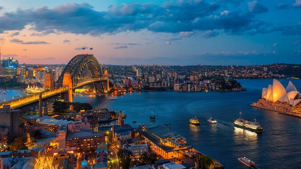 The cityscape of Sydney, Australia reveals a long bridge extending across a harbor to a bustling metropolis