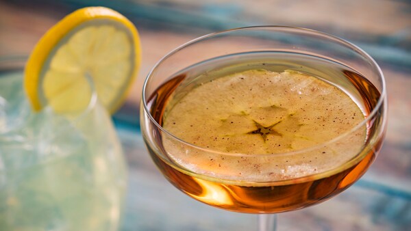 A glass of water topped with a slice of lemon next to a cocktail