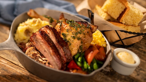 Una cesta de pan de maíz y una sartén con falda, pollo, puré de papas, judías verdes y maíz