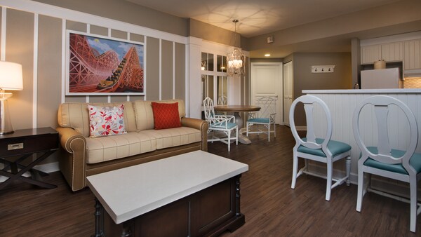 Une chambre avec un canapé, une table basse, 2 chaises, art mural, une lampe suspendue, une table à manger avec 2 chaises et une cuisine ouverte