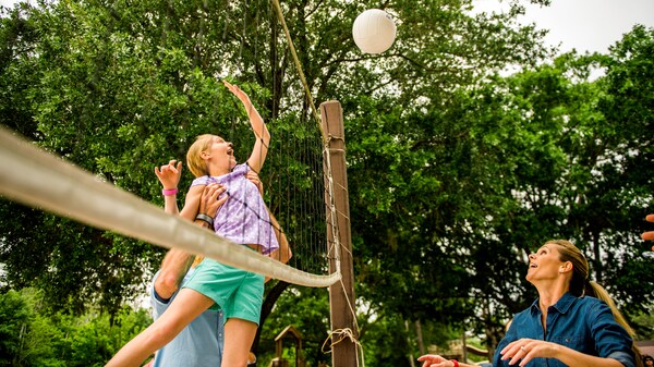 Un hombre levanta a su hija para que golpee una pelota de vóley a través de una red